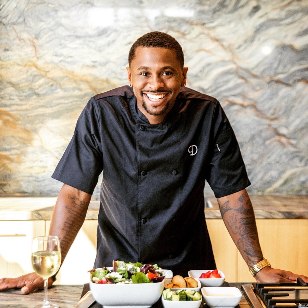 Chef Phillip Dewayne smiling for the camera as he stands over food he is presenting